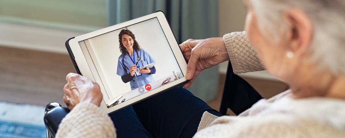 An elderly patient participating in a telehealth call with a nurse on an iPad.
