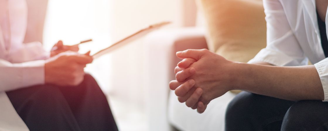 Counseling session with patient clasping own hands while counselor takes notes