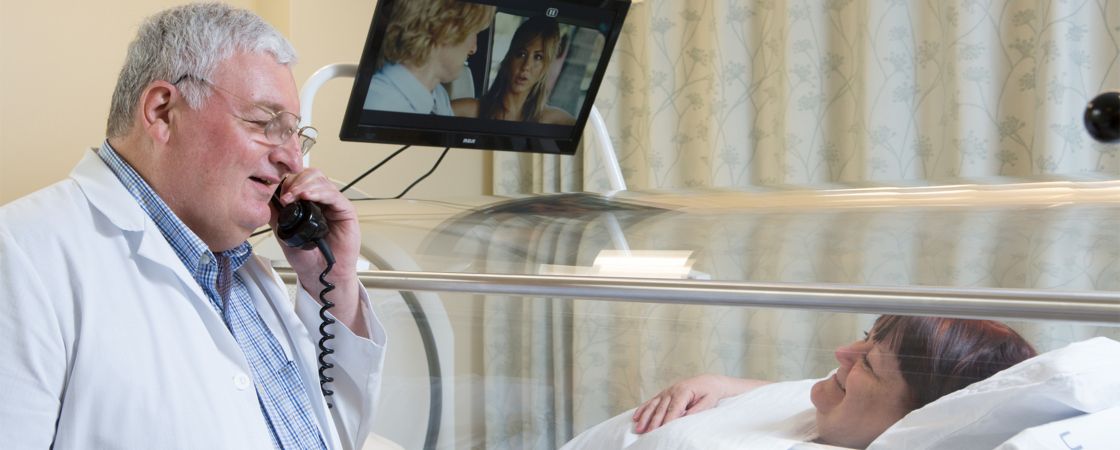 Doctor speaking on phone next to patient in hospital bed