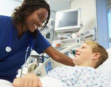 Nurse smiling at young boy in hospital bed