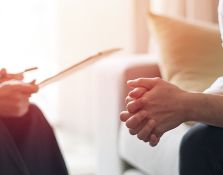 Person with clasped hands across from someone with a clipboard