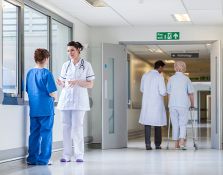 Doctor walking with elderly patient and two nurses talking in hallway