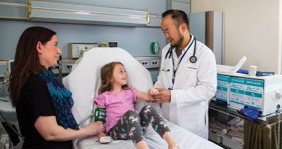 Mother next to girl in hospital bed being examined by doctor