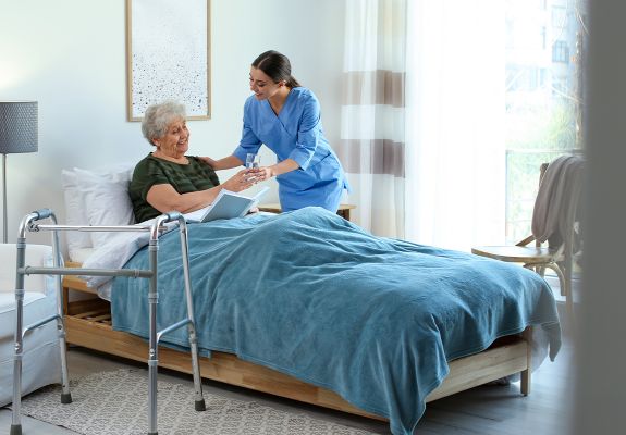 Nurse handing glass to elderly patient in bed