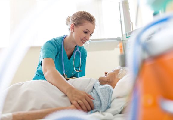 Nurse tucking in patient in hospital bed