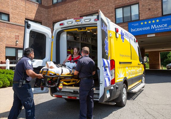 Person on stretcher being lifted into an ambulance by two EMTs